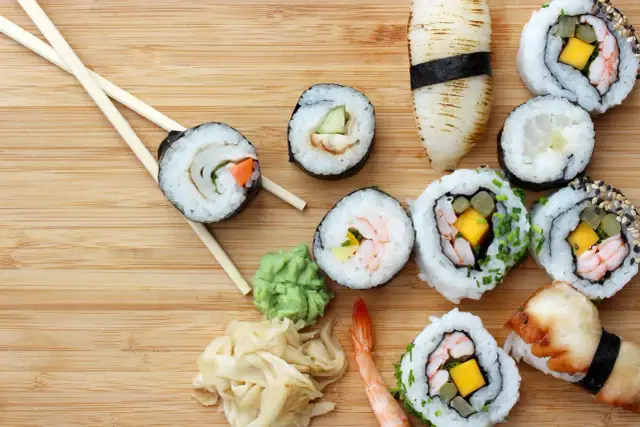 Różnorodne sushi z krewetkami, mango i warzywami, pałeczki, wasabi i marynowany imbir na drewnianym tle.