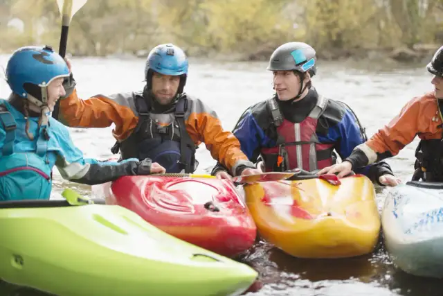 Ludzie w kaskach i kamizelkach ratunkowych w kajakach na wodzie.