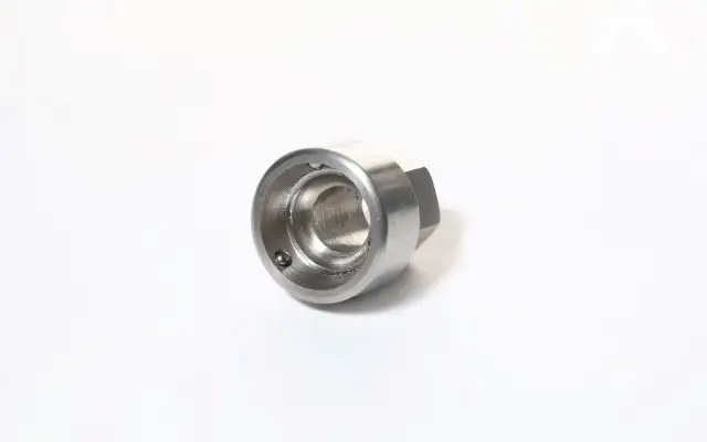 Metalowy, sześciokątny element z otworem w środku, z widoczną kulką wewnątrz. To uniwersalny klucz do śrub zabezpieczających.