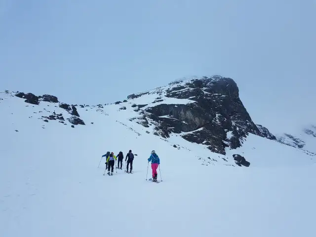 Grupa narciarzy podchodzi pod Kościelec zimą. W tle majestatyczna, ośnieżona góra.