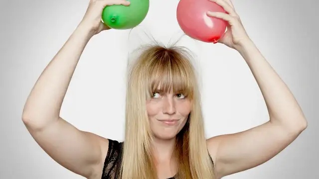 Dziewczyna z zielonym i różowym balonem nad głową, jej elektryzujące się włosy sterczą na wszystkie strony.