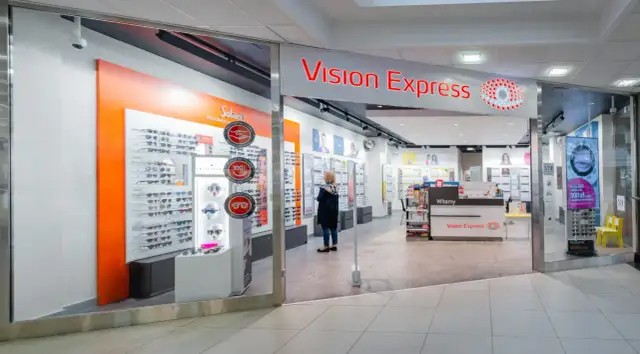 Sklep Vision Express z ekspozycją okularów i kobietą przeglądającą ofertę.