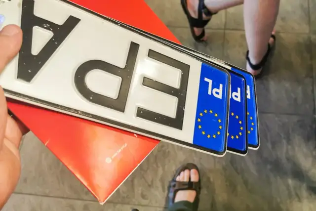 Kilka nowych tablic rejestracyjnych PL leży na czerwonym podkładzie.