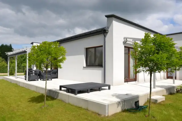 Nowoczesny biały dom z płaskim dachem, tarasem i zielonym ogrodem.