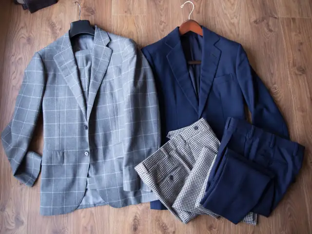 Dwa garnitury: jeden w kratę, drugi granatowy, leżą na drewnianej podłodze.