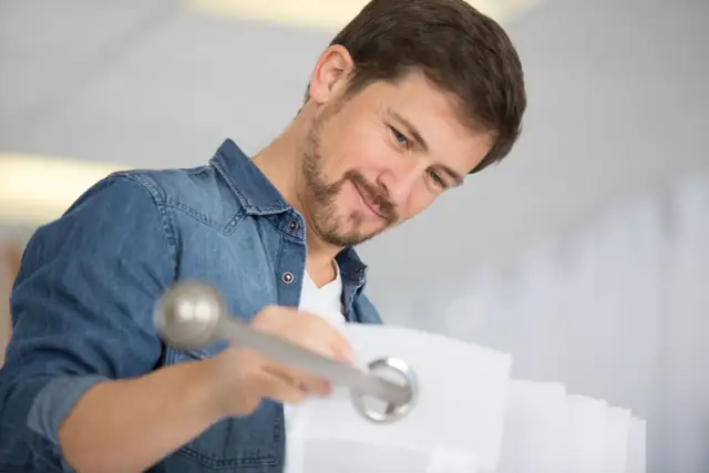 Mężczyzna w dżinsowej koszuli montuje karnisz, przekładając go przez kółka zasłony.