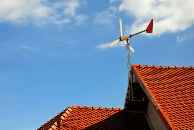 Mała elektrownia przydomowa na tle błękitnego nieba z chmurami. Wirnik turbiny wiatrowej obraca się, dostarczając czystą energię.