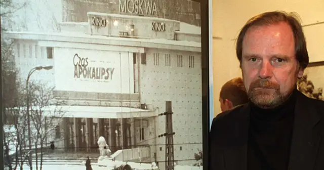 Chris Niedenthal obok plakatu filmu "Czas Apokalipsy" z kinem Moskwa w tle.