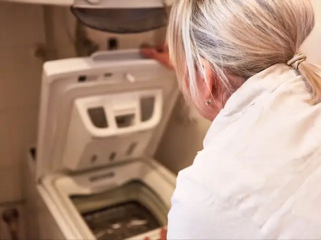 Kobieta otwiera pralkę, przygotowując się do jej czyszczenia. Proste kroki, jak wyczyścić pralkę, zapewnią jej dłuższą żywotność.
