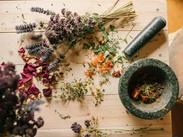 Suszone zioła na ból głowy: lawenda, nagietek, róża i dziurawiec w moździerzu.