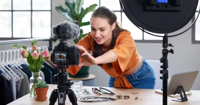 Kobieta nagrywa film na kamerze, otoczona akcesoriami i ubraniami.