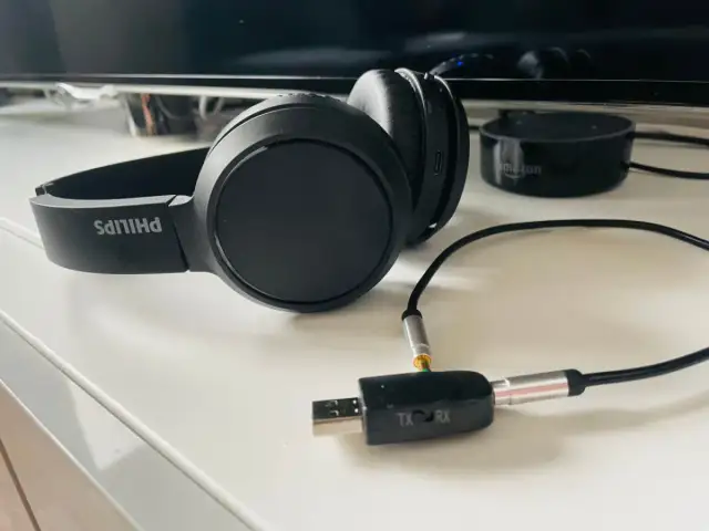 Czarne słuchawki Philips podłączone do adaptera Bluetooth TX/RX na białym blacie.