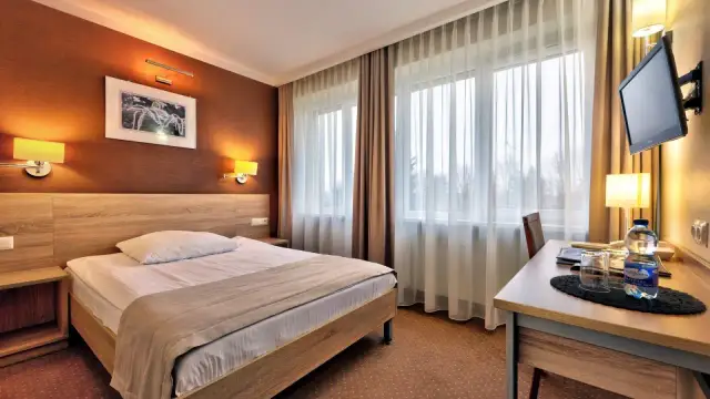 Przytulny pokój hotelowy w Białymstoku z wygodnym łóżkiem, biurkiem i telewizorem.