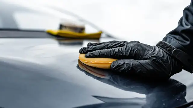 Ręka w czarnej rękawiczce rozprowadza produkt na lakierze. Czy to wosk czy ceramika, efekt jest olśniewający.