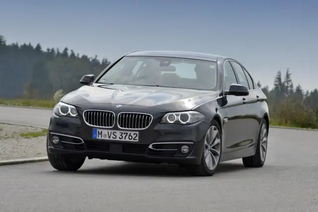 Ciemnoszary sedan BMW F10 na drodze, z widokiem na las. Idealne wymiary dla komfortowej podróży.