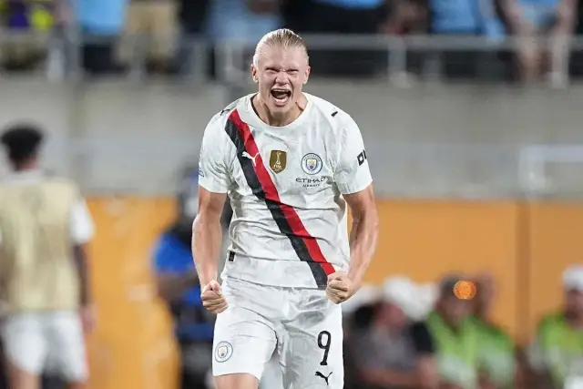 Piłkarz Manchesteru City, Erling Haaland, w białej koszulce z czerwono-czarnym pasem, świętuje bramkę.