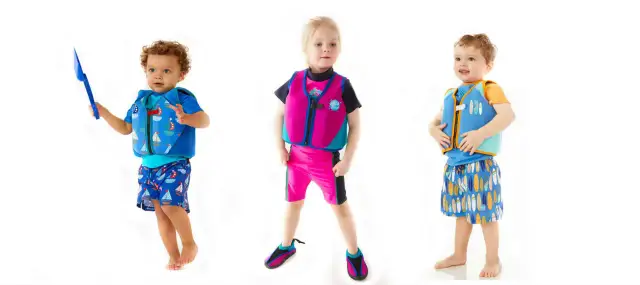 Trójka dzieci w kolorowych kamizelkach do pływania. Chłopiec po lewej trzyma łopatkę, dziewczynka w środku ma różową kamizelkę, a chłopiec po prawej niebieską.