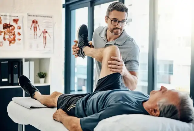 Fizjoterapeuta wykonuje ćwiczenia z pacjentem leżącym na kozetce.