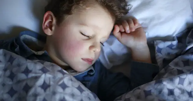 Mały chłopiec śpi pod kołdrą. Może nawet mówi przez sen, opowiadając o swoich snach.