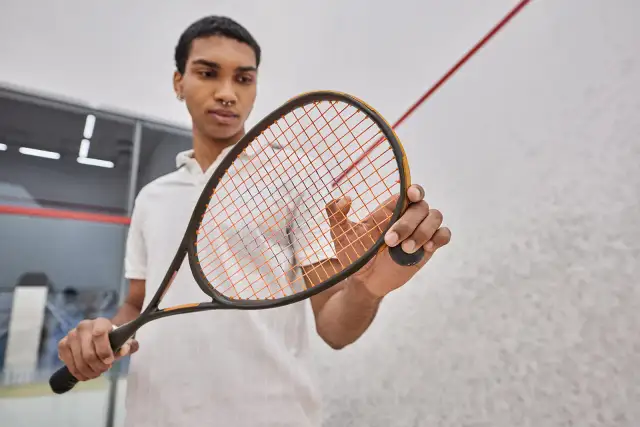 Mężczyzna trzyma rakietę do squasha z pomarańczowymi naciągami.