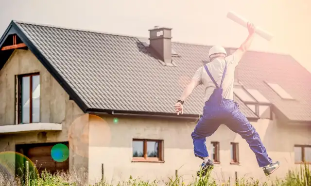 Budowniczy w skoku z planami przed budynkiem gospodarczym.