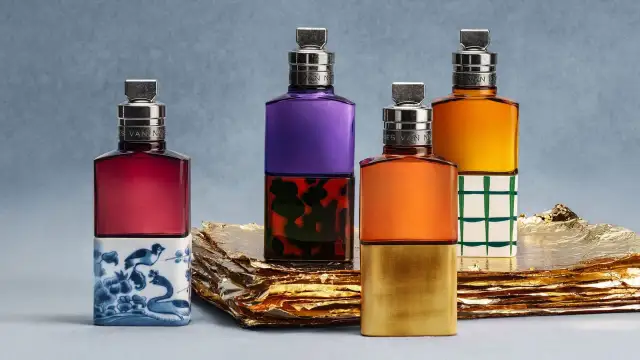 Vier bunte Parfumflaschen mit silbernen Verschlüssen auf goldenem Untergrund.