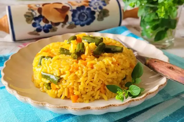 Ryż z curry, marchewką i fasolką szparagową na talerzu, ozdobiony ziołami.