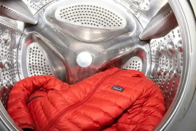 Czerwona kurtka z pierza czeka w bębnie pralki. Dowiedz się, jak prać kurtkę z pierza, by zachowała swoje właściwości.
