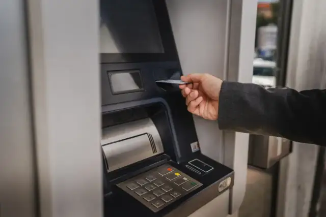 Dłoń wsuwa kartę do bankomatu, by sprawdzić, ile można wypłacić.