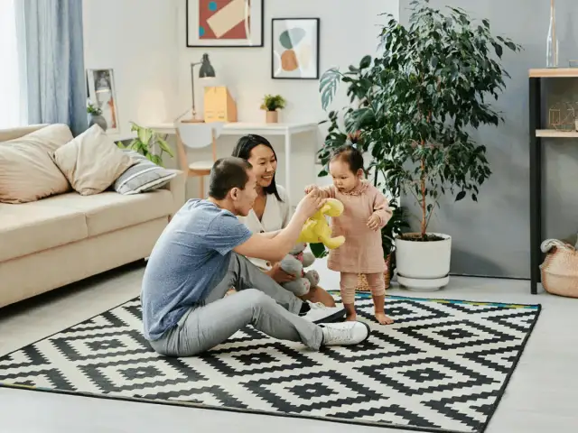 Rodzice bawią się z dzieckiem na dywanie w salonie.