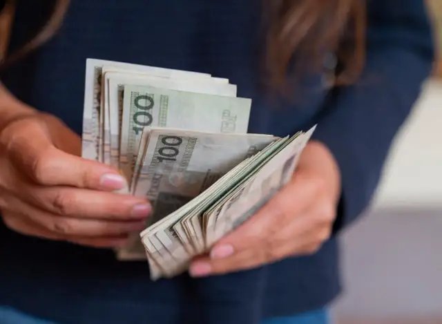 Dłonie liczą banknoty 100 zł. Czy to kwota, która ujawnia ile płacą w ukrytej prawdzie?
