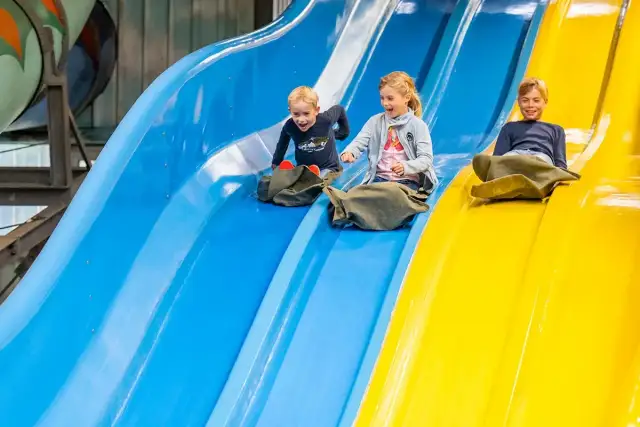 Drei Kinder rutschen lachend auf bunten Wasserrutschen.