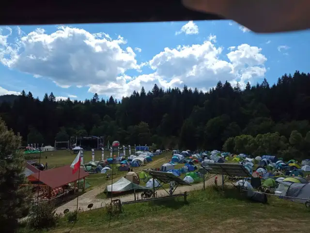 Pole namiotowe na festiwalu w Solinie. Tysiące namiotów pod błękitnym niebem z chmurami, w tle las i scena festiwalowa.