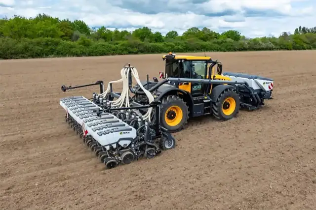 Żółty traktor z przyczepionym nowoczesnym siewnikiem do nawozu ogrodowego pracuje na pustym polu.