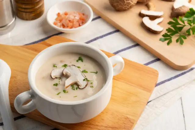 Kremowa zupa grzybowa z plasterkami grzybów i natką pietruszki w białej miseczce.