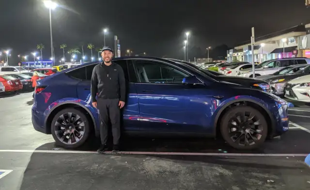 Mężczyzna stoi obok swojego niebieskiego Tesli. Zastanawiasz się, ile waży Tesla? Ten model waży około 2 ton.