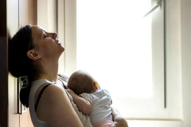 Zmęczona mama tuli śpiące dziecko. Czas po porodzie bywa trudny, ale miłość do malucha daje siłę.