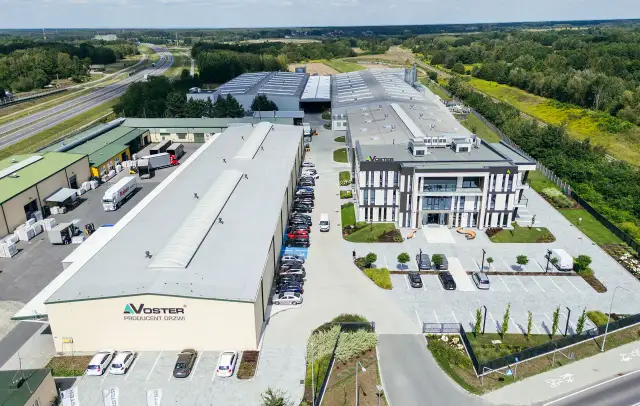 Nowoczesny kompleks produkcyjny Voster producent drzwi, z drogą szybkiego ruchu w tle.