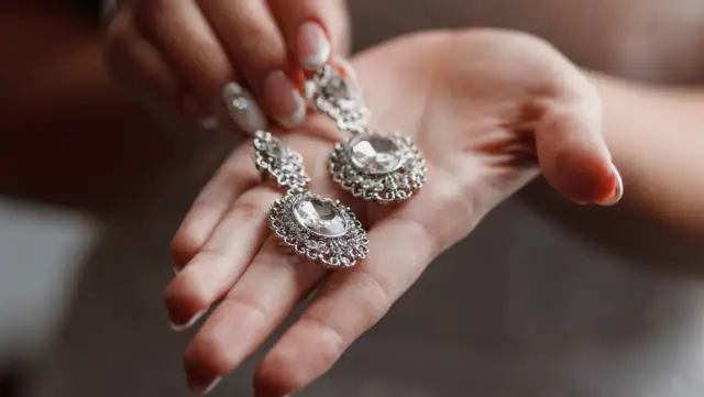 Dłoń trzymająca błyszczące, srebrne kolczyki z cyrkoniami.