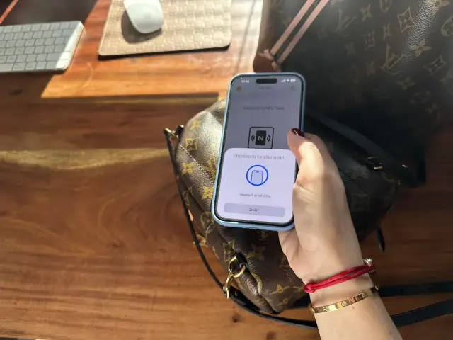 Dłoń trzymająca telefon z aplikacją NFC nad torebką Louis Vuitton.