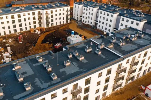 Budowa osiedla mieszkanie plus w trakcie. Nowe bloki z balkonami, plac budowy z koparką i materiałami.