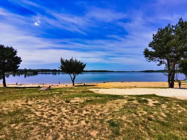 Słoneczny dzień nad jeziorem Pławniowice. Ludzie odpoczywają na piaszczystej plaży, ciesząc się błękitem nieba i spokojną wodą.