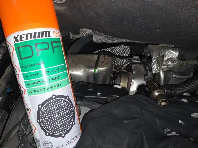 Bouteille de nettoyant FAP Xenum à côté d'un capteur et de pièces de moteur.