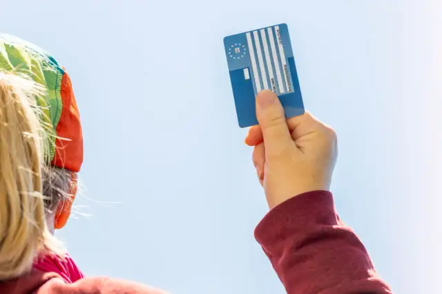 Karta EKUZ dla dziecka – jak wyrobić? Ręka trzyma niebieską kartę EKUZ na tle błękitnego nieba.