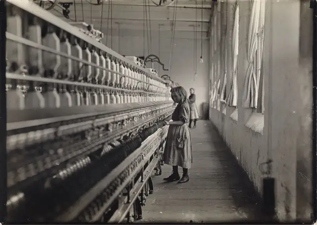 Dziewczynka pracuje przy maszynie w fabryce, jak na zdjęciach Lewis Hine. W tle widać inną pracownicę.