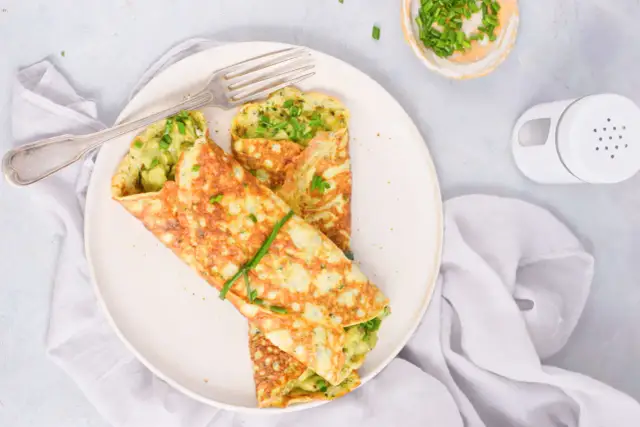 Omlet z awokado i szczypiorkiem na talerzu, obok widelca i miseczki ze szczypiorkiem.