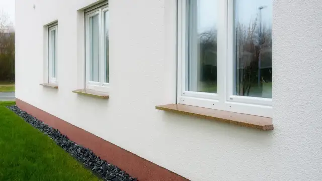 Eleganckie, kamienne parapety przy białym domu. Zastanawiasz się, jak przedłużyć parapet? Ten przykład pokazuje, jak estetycznie można to zrobić.