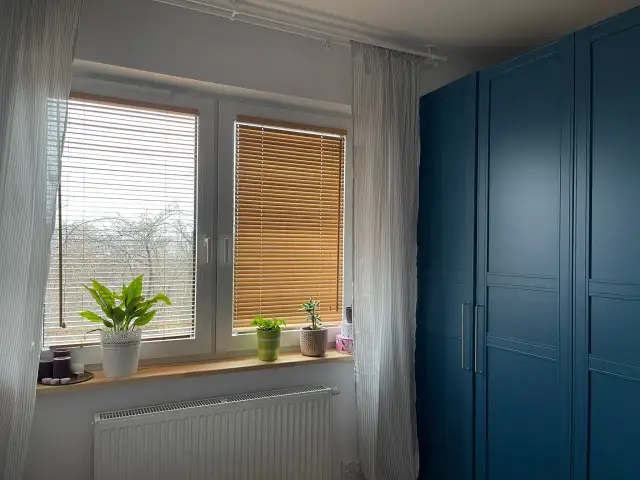 Eleganckie żaluzje bambusowe aranżacje okna, tworzące przytulną atmosferę. Obok niebieska szafa.
