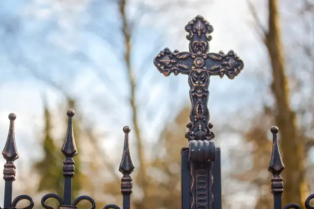 Ozdobny krzyż na tle nieba i drzew.