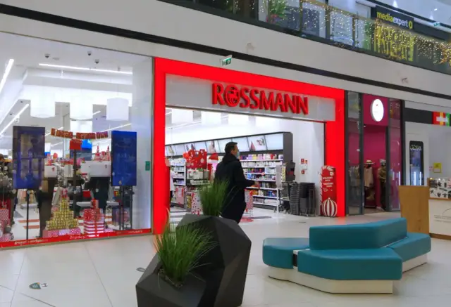 Wejście do drogerii Rossmann w centrum handlowym, z widocznymi promocjami i wystrojem świątecznym.